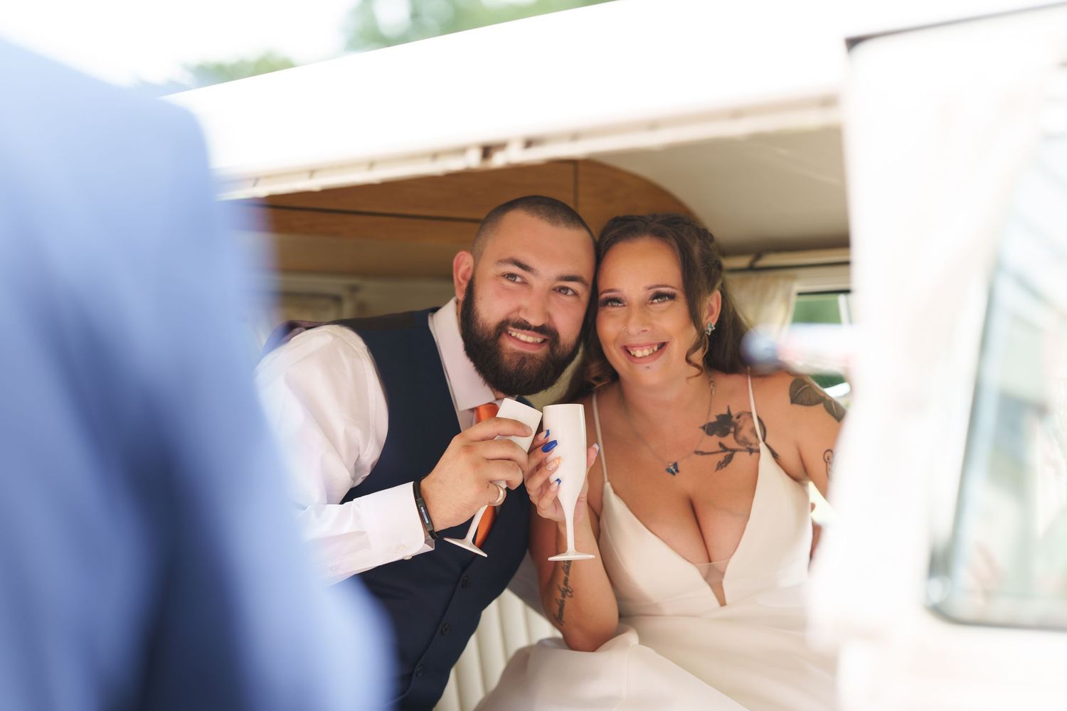 A cheerful couple in wedding attire smiling while posing inside what appears to be a vehicle.