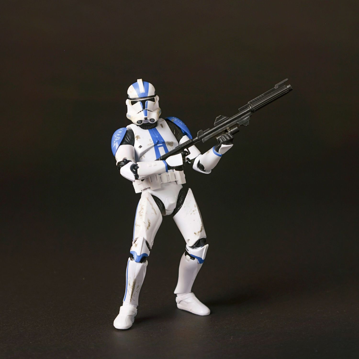 A Star Wars clone trooper action figure with blue markings holds a blaster rifle against a dark background.