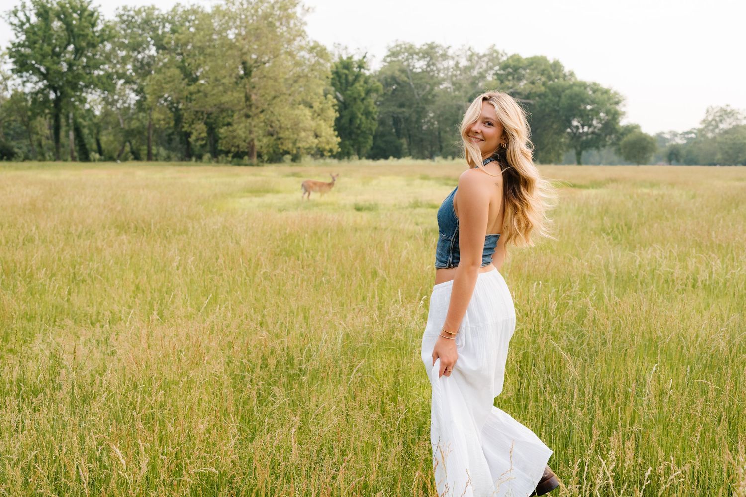White flowy dress contrasts against golden tall grass field at sunset, creating a dreamy pastoral scene.