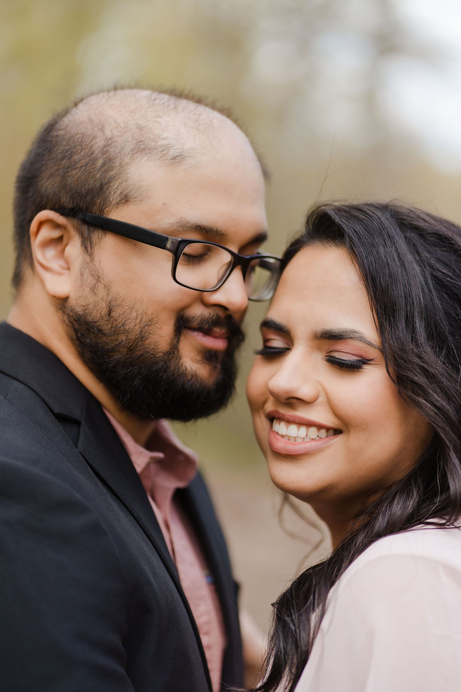 A romantic couple in formal attire share an intimate moment outdoors, with the woman smiling and eyes closed.