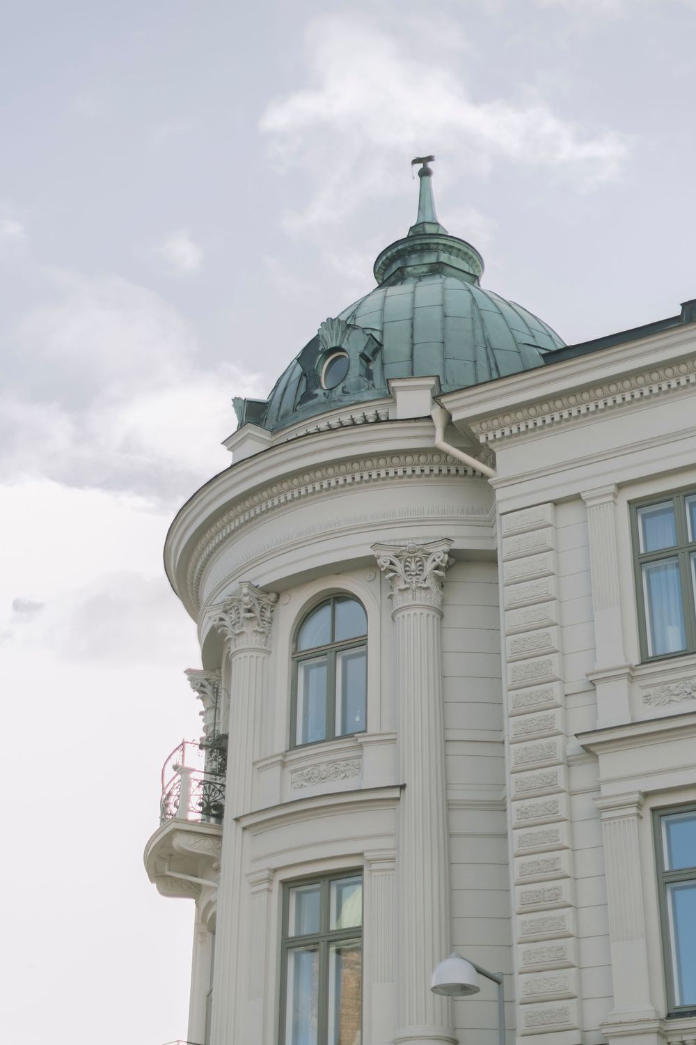 Elegant white neoclassical building with green copper dome and ornate columns against cloudy sky.