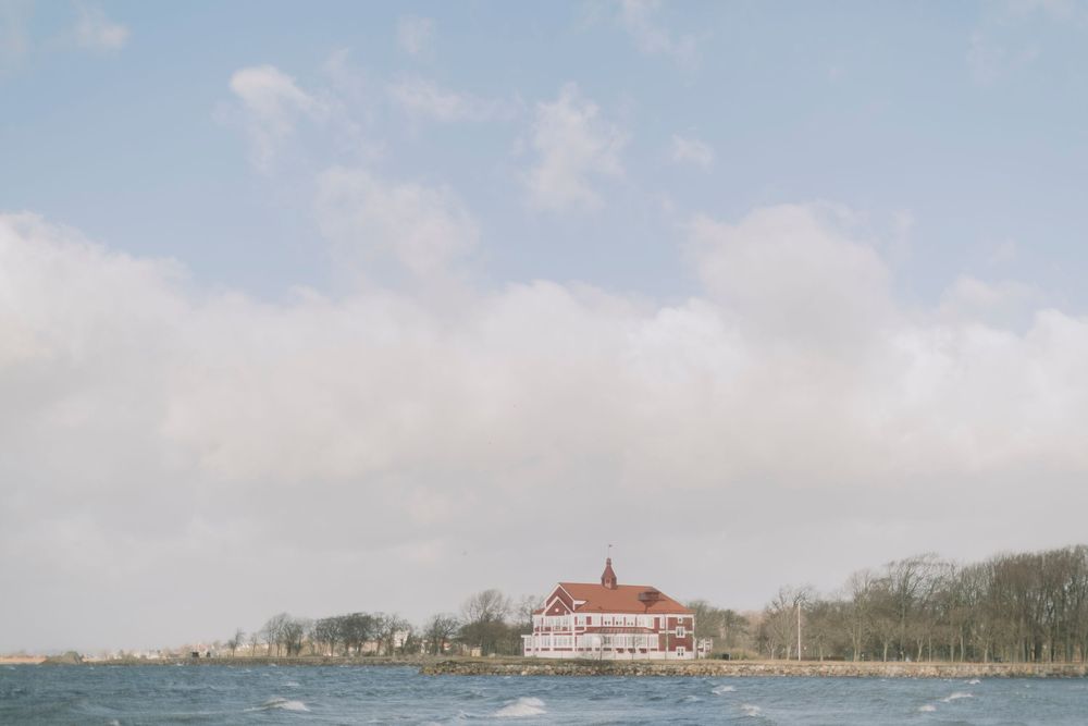 Charming red-roofed waterfront mansion on a small peninsula surrounded by choppy blue water.