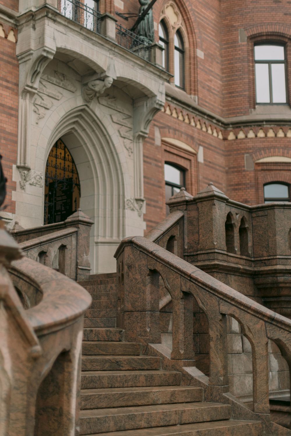 Grand Gothic red brick building entrance with ornate stone staircase and arched doorway details.