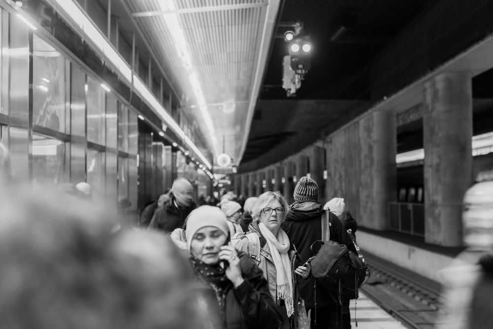 Black and white photo of women in winter hats standing on a busy train platform at night.