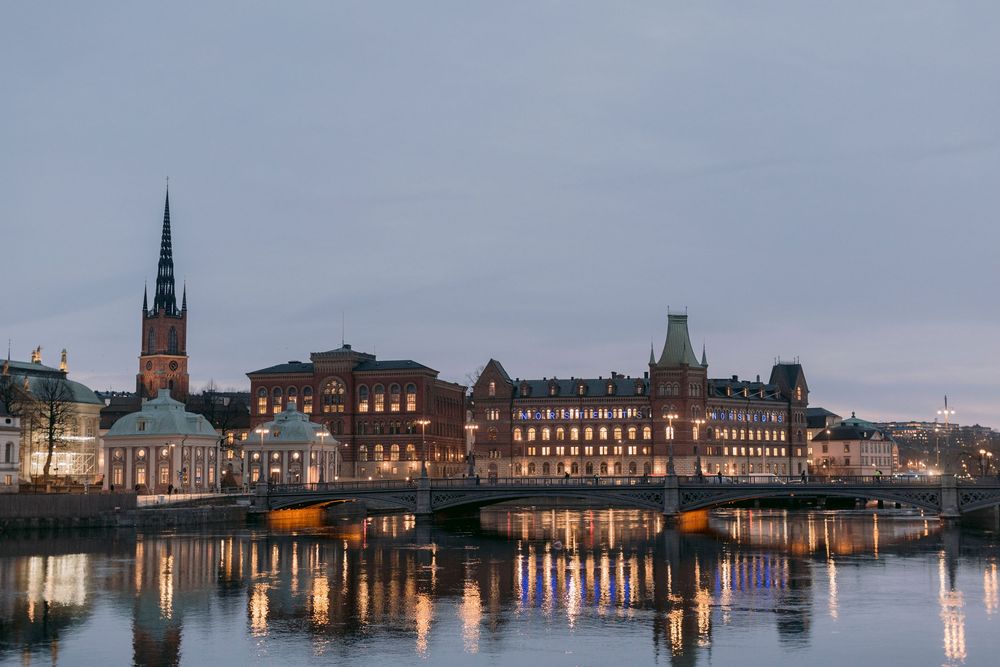 Panoramic twilight view of historic Malmo city waterfront with illuminated buildings reflecting in river.