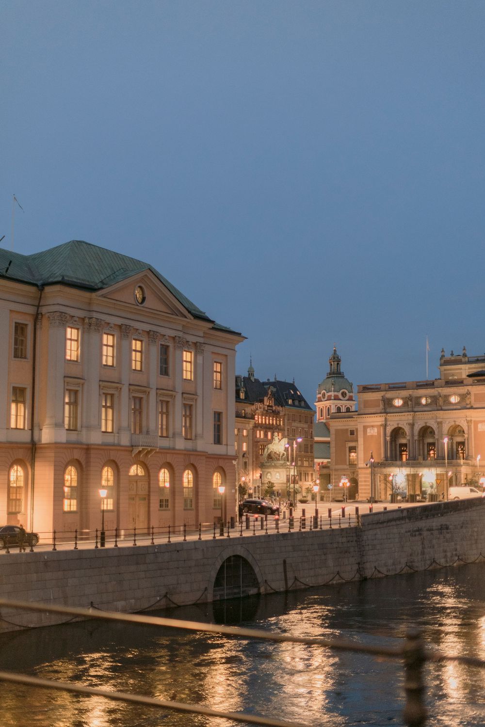 Historic neoclassical buildings along Stockholm waterfront canal beautifully lit at blue hour evening.