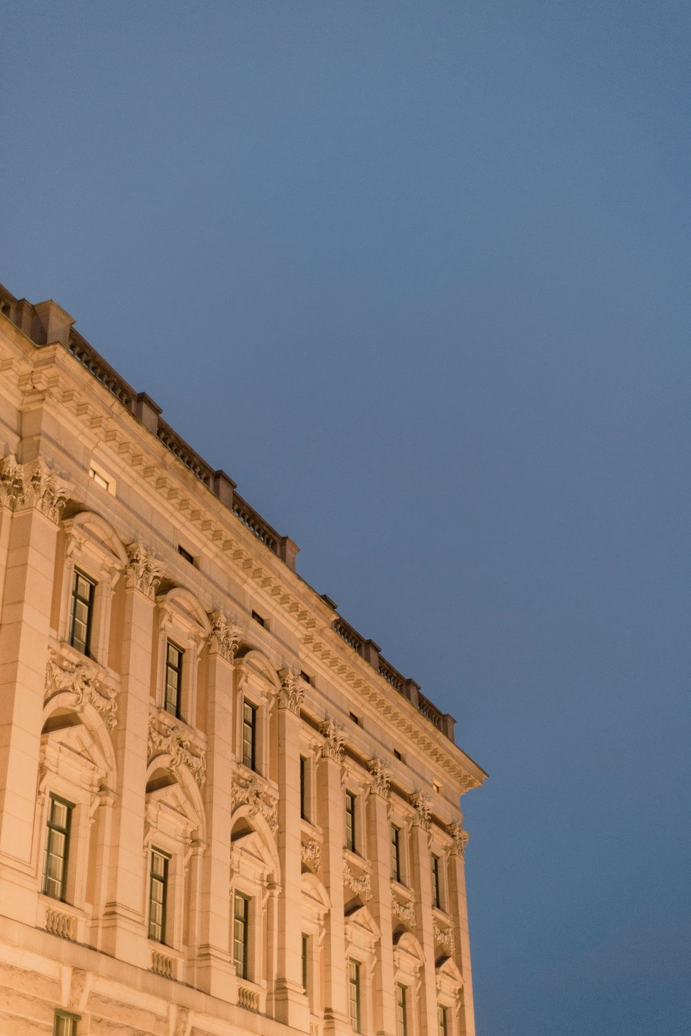 Close-up of ornate neoclassical building facade with decorative cornices against clear blue twilight sky.