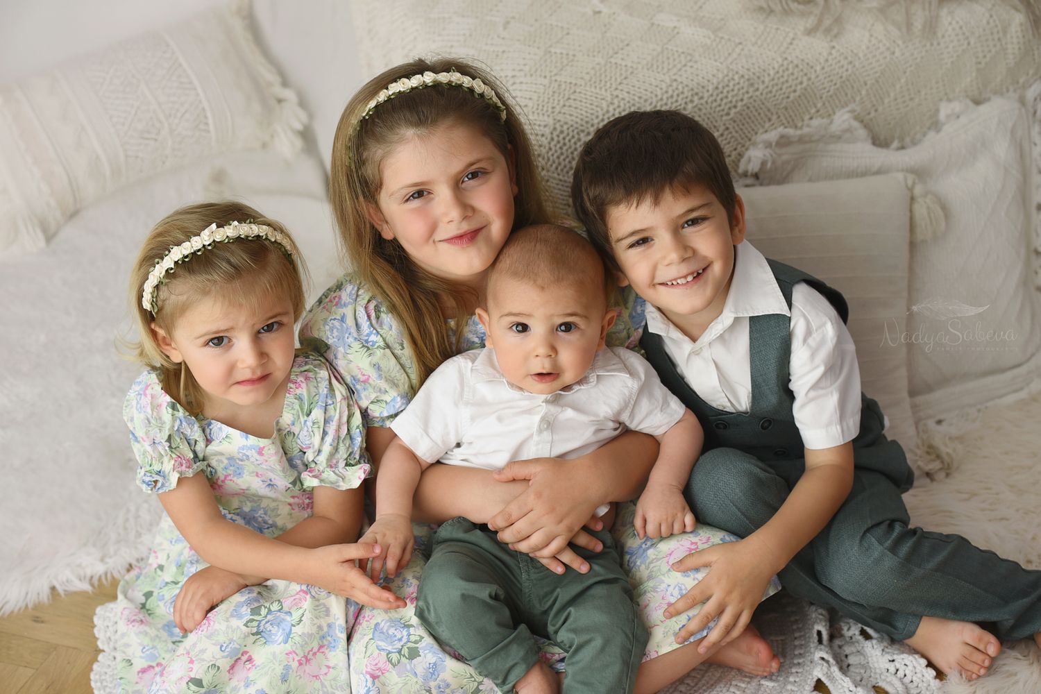 Three children sit on grass at an outdoor birthday party with a small cake and single candle.