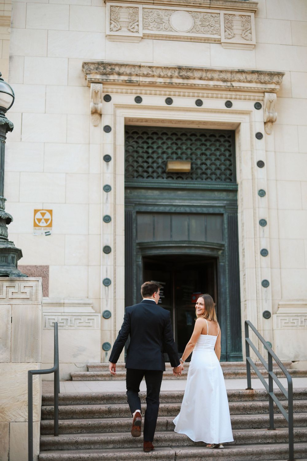 A couple in wedding attire ascending stone steps towards an ornate blue doorway of a historic building.