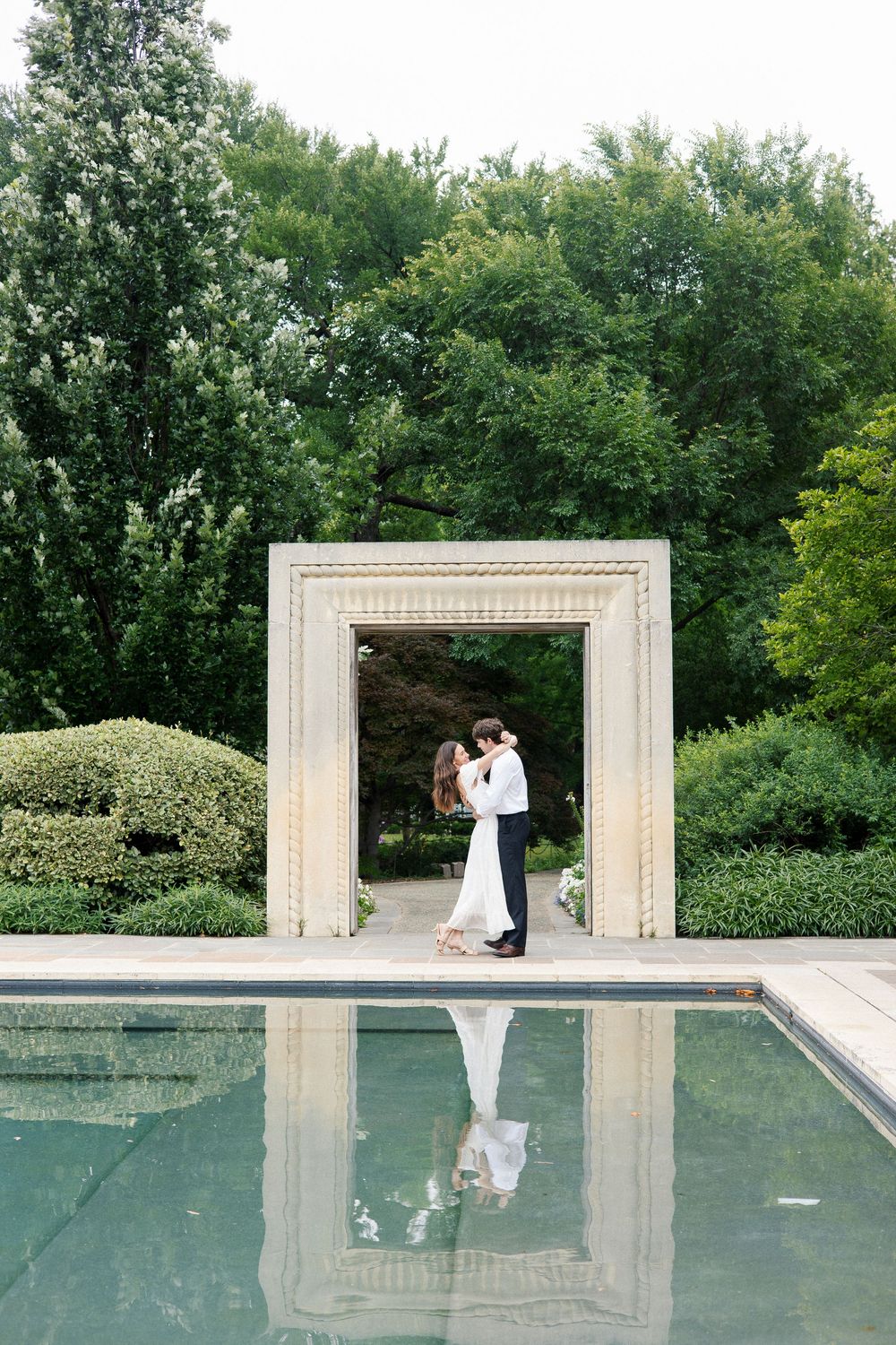 A romantic moment captured through architectural frames beside a reflective pool.