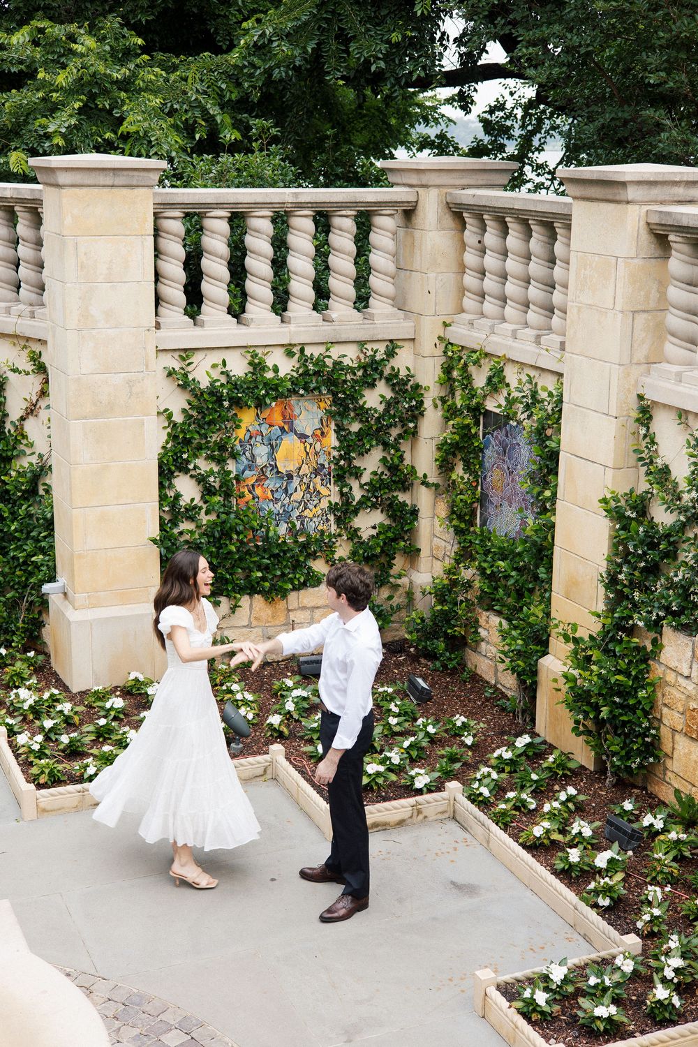 A couple dancing in a beautiful garden terrace with ornate stone balustrades and floral decorations.