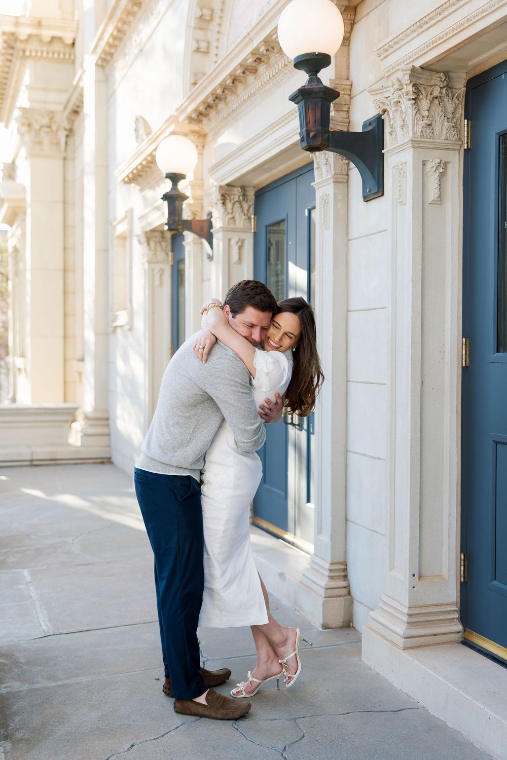 Couple sharing a warm embrace outside an elegant building with ornate columns and blue doors.