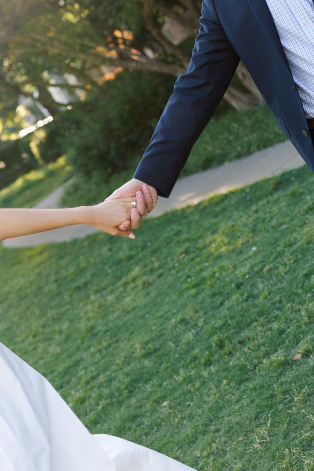 Bride and groom holding hands on green grass, bride in white gown and groom in navy suit, outdoor wedding photo.