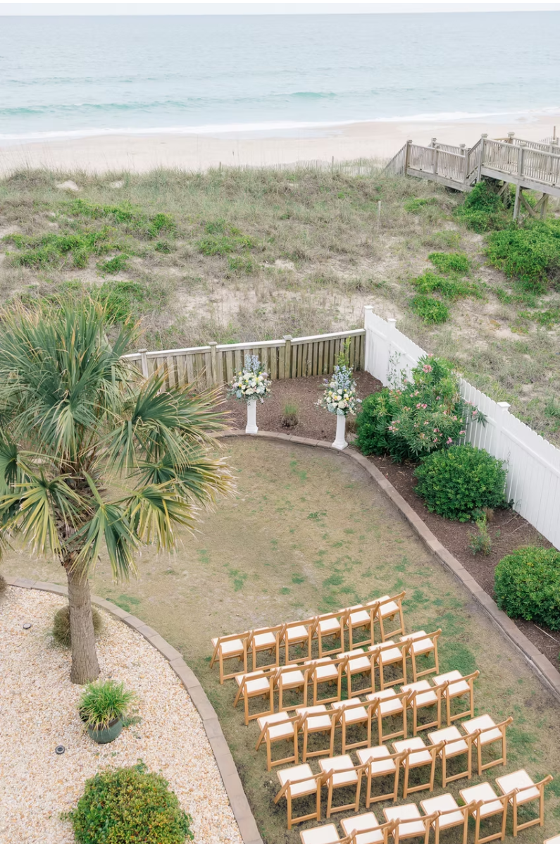 Aerial view of a beachfront wedding ceremony setup with wooden chairs arranged in rows by a coastal palm tree.