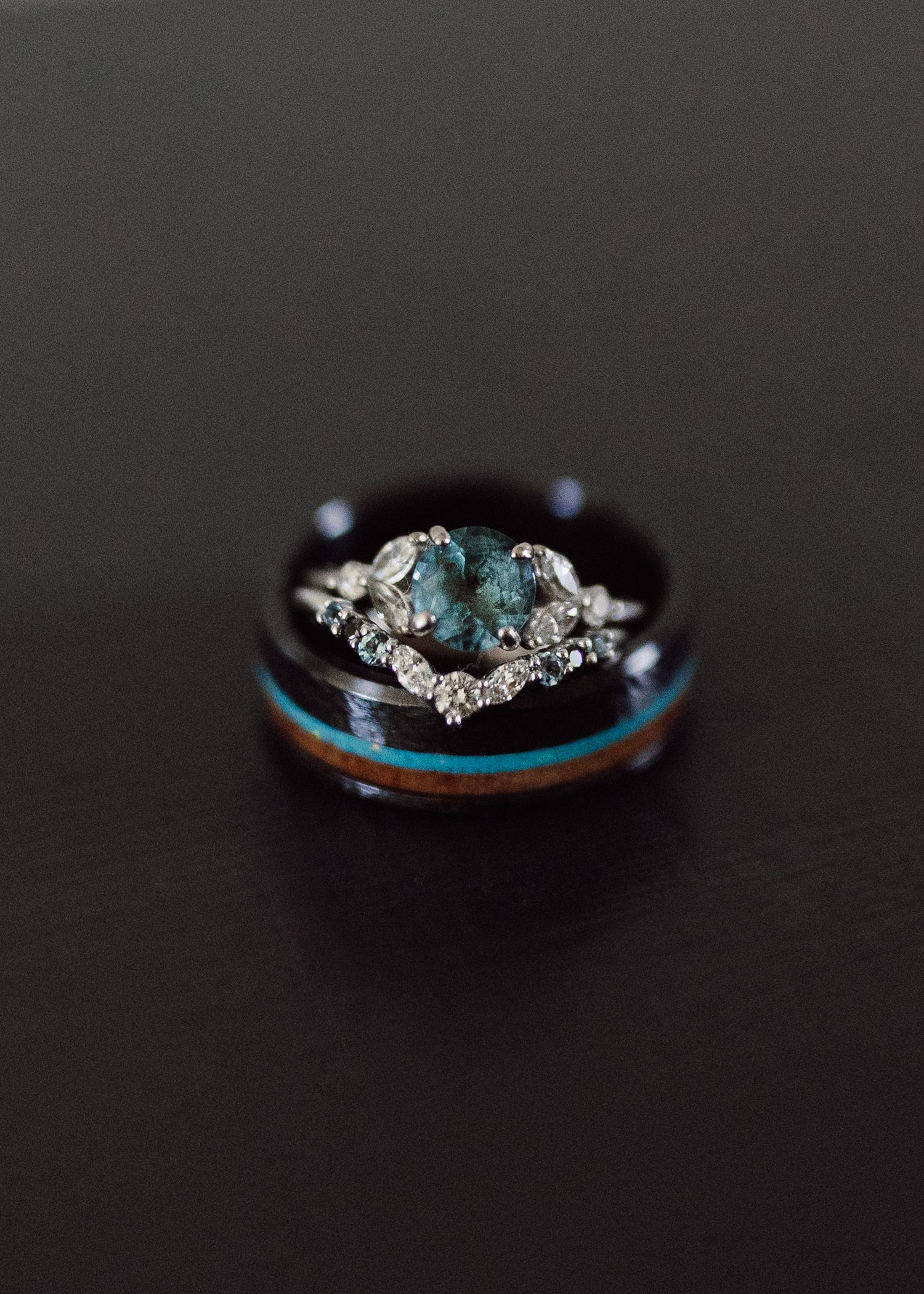 An elegant engagement ring featuring aqua stones and diamonds on a wooden band.
