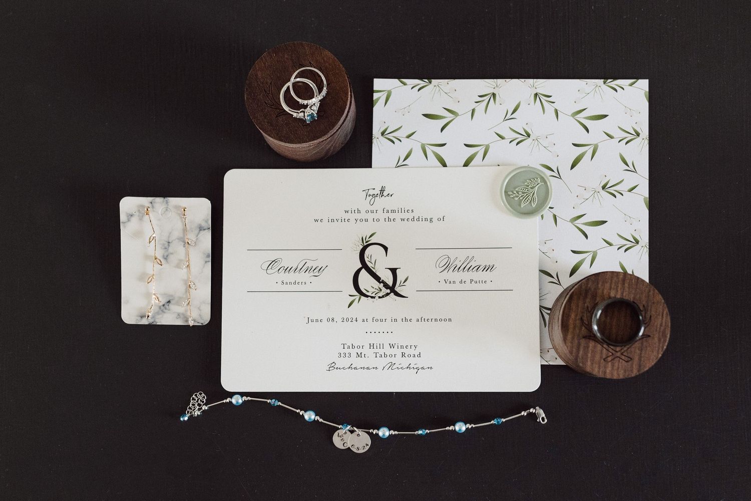 Wedding invitation suite with wooden ring boxes and floral design elements.