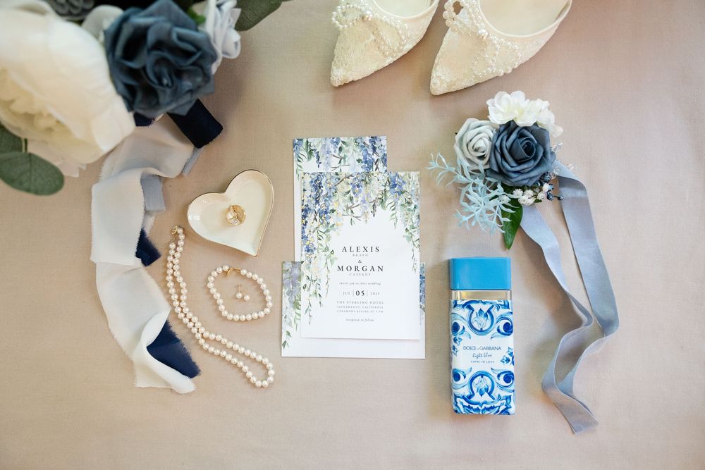 Wedding invitation suite with floral blue and white designs arranged alongside silk ribbons and white flowers.
