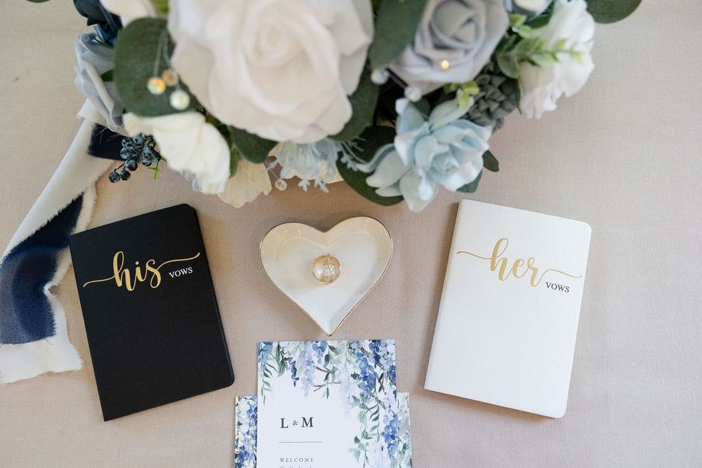 Elegant wedding details featuring white roses, blue accents, and calligraphy invitations on a light background.