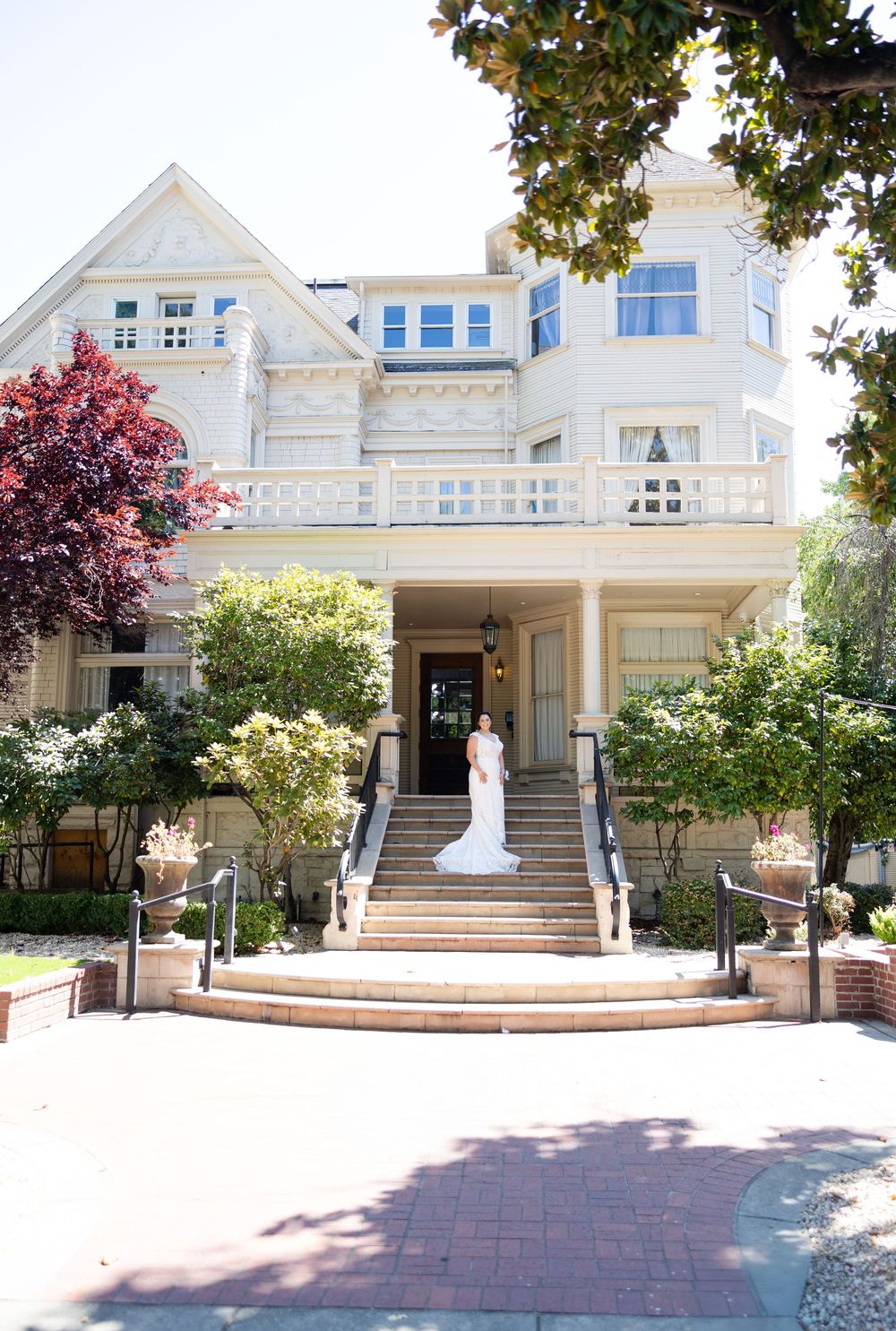 Elegant white Victorian mansion with grand staircase entrance adorned with beautiful landscaping and red maple trees.