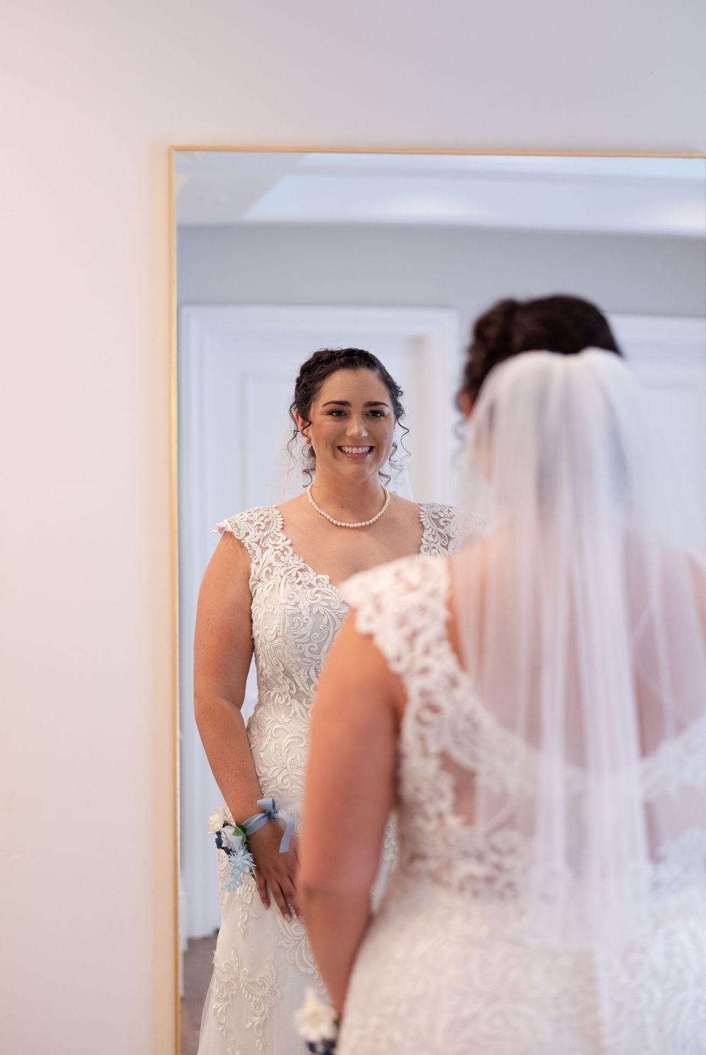A reflection shows a bridal gown being fitted in an elegant mirror.