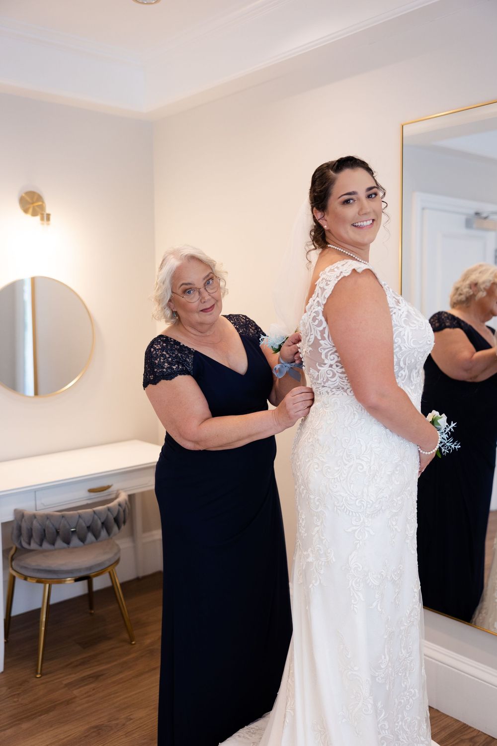 A wedding dress being prepared and adjusted in a bright dressing room with mirrors.