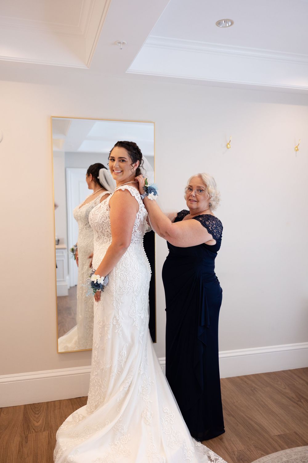 Wedding preparation scene showing dress fitting and final adjustments in a bright room with mirror.