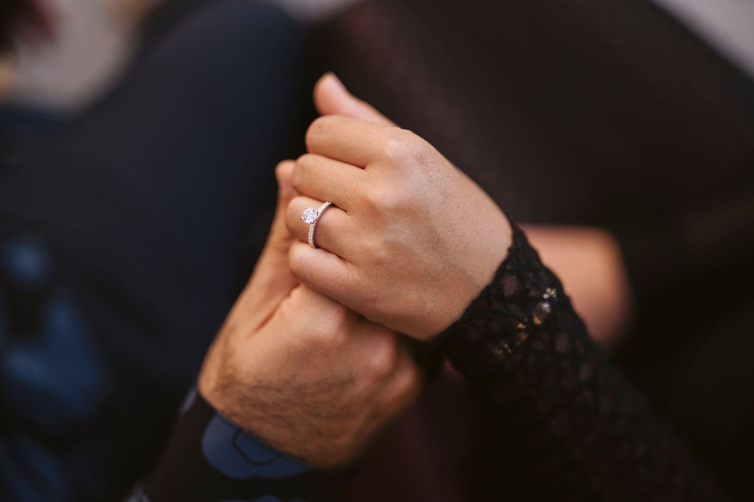 Le mani di due giovani fidanzati si stringono mettendo in evidenza l'anello di fidanzamento.