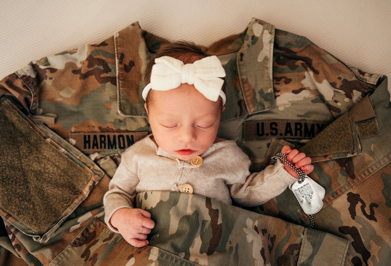 A small baby lies on military camouflage uniforms and gear arranged in a gentle loving composition.
