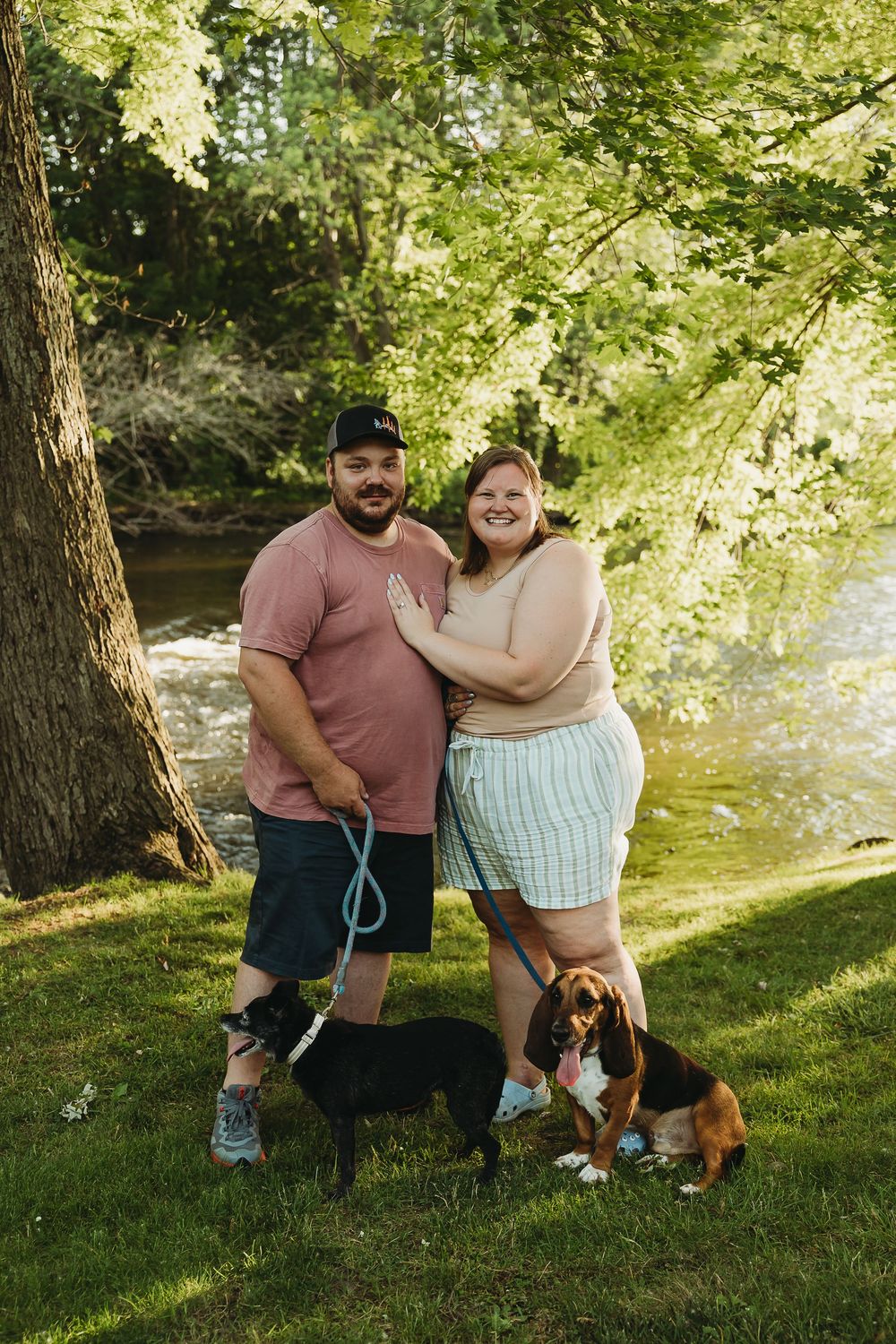 Couple laughing together outdoors in a sunny park with their dog on a warm summer day.