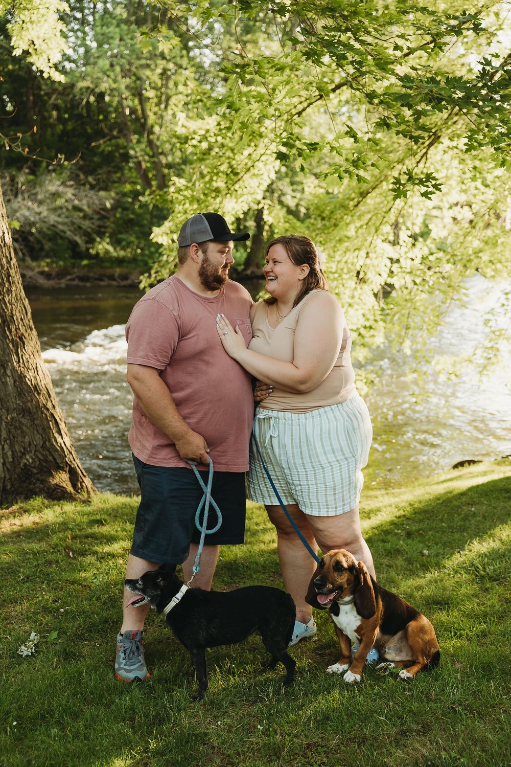 Couple sharing a tender moment in a sunlit park with their Bernese Mountain Dog enjoying a summer afternoon together.