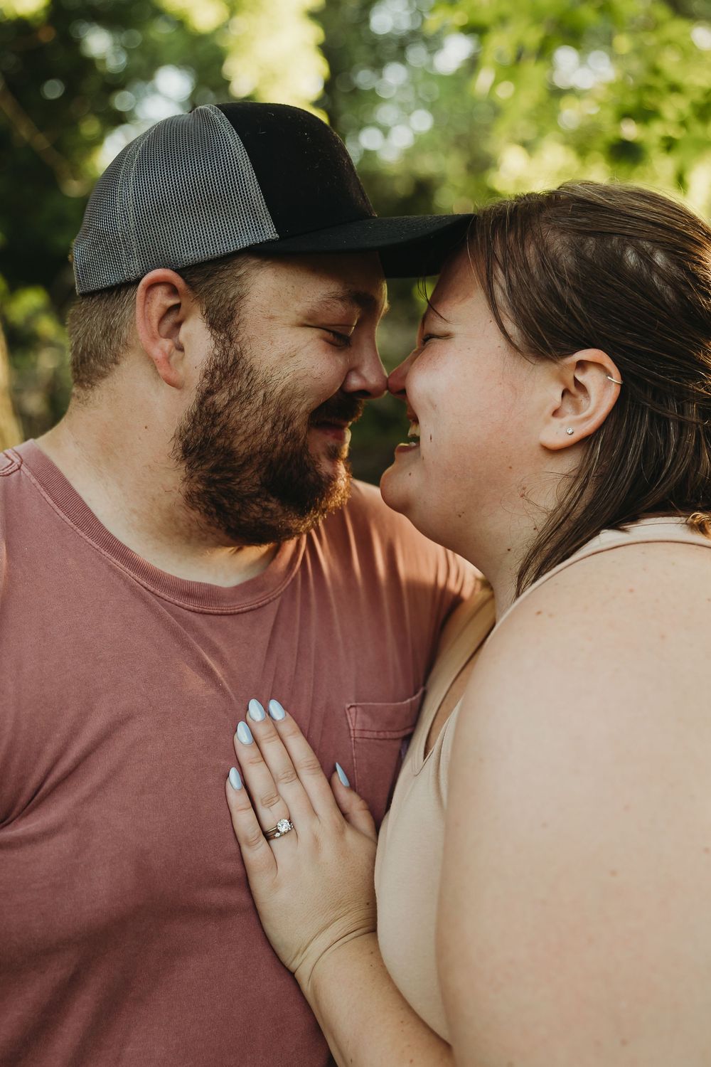 A loving couple shares an intimate close-up moment together outdoors in natural lighting, with greenery in the background.