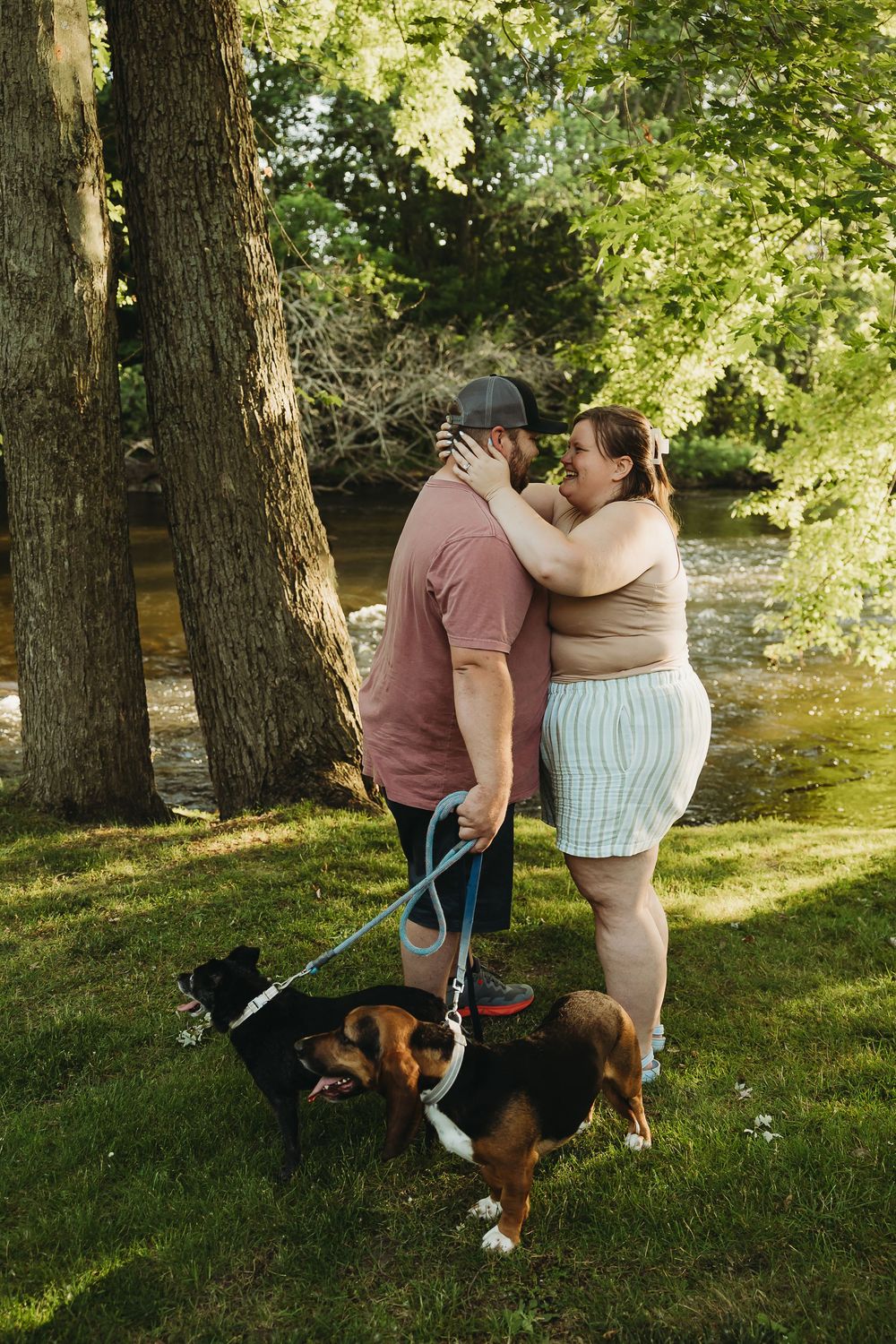 A couple shares an intimate moment while walking their Beagle dog near a stream on a sunny summer day.
