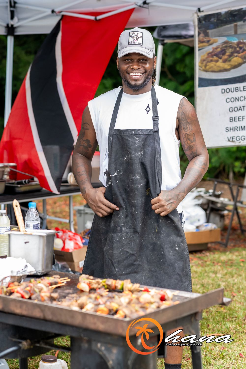 Chefs in black aprons grilling skewers of meat and seafood at an outdoor food festival or barbecue event.