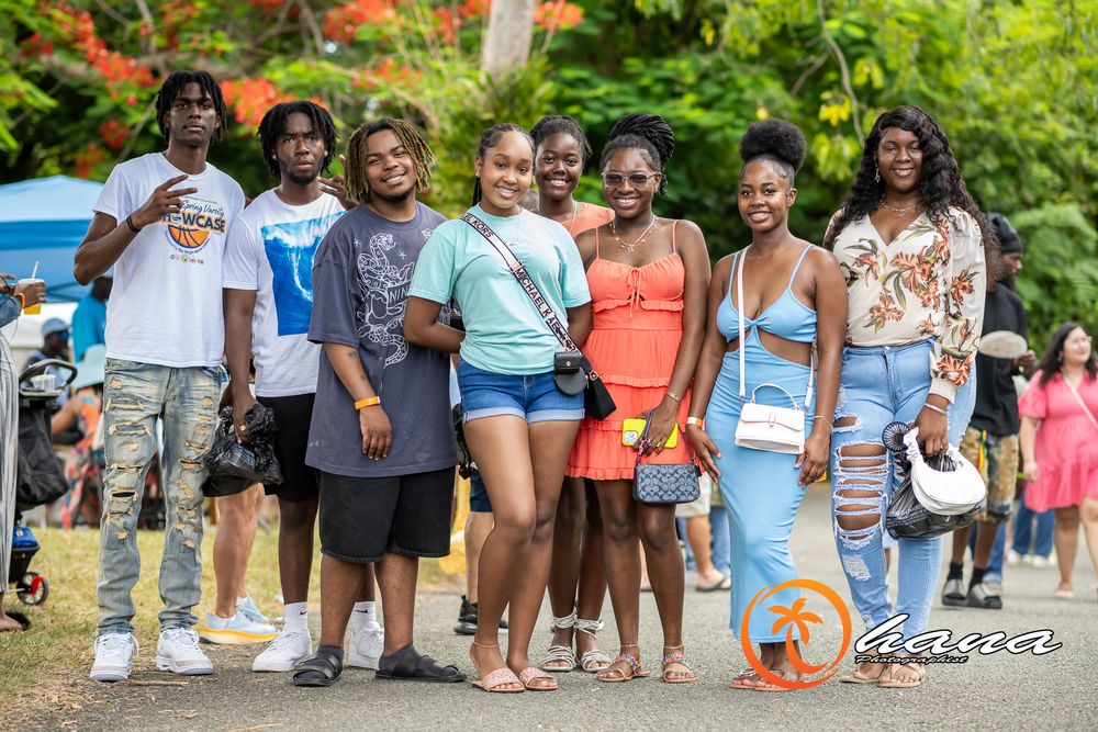 A group of people smile and pose together outdoors on a sunny day at what appears to be a summer gathering.