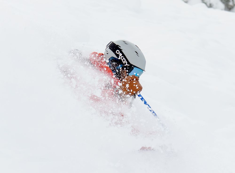 A skier carves through deep powder snow creating a dramatic spray while descending down a pristine mountain slope.