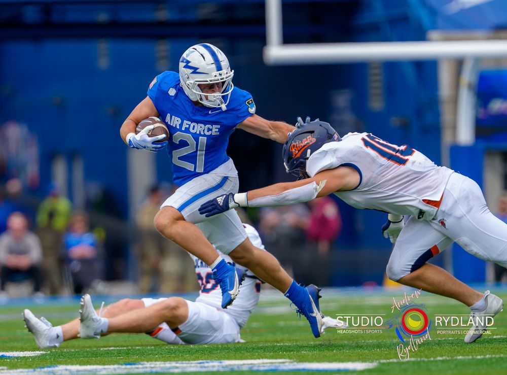 Football player dives and stretches out to make a play during an intense game on a blue turf field.
