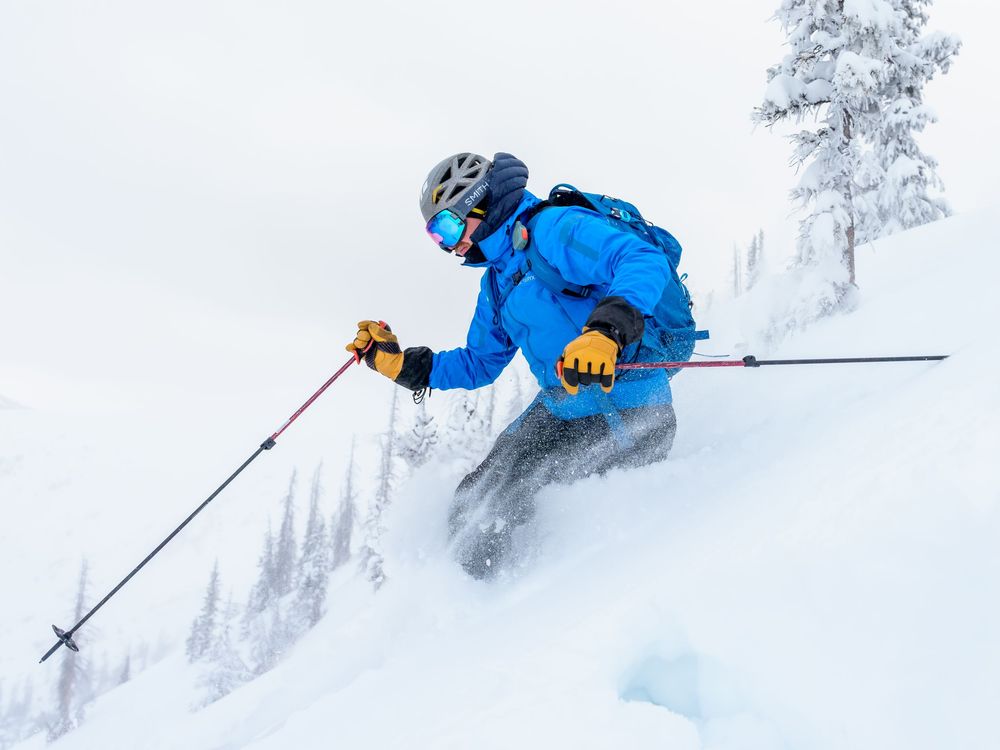 A skier in bright blue gear carves through deep powder snow on a steep mountain slope during winter.