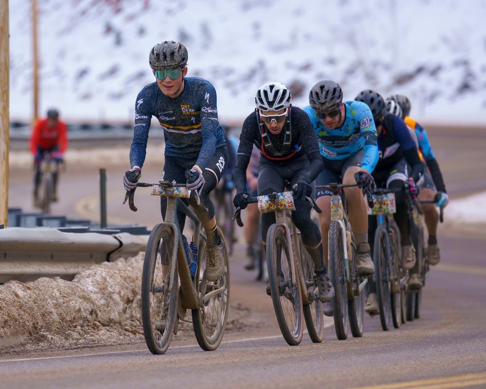 Cyclists riding in a line on a snowy mountain road during a winter cycling competition.