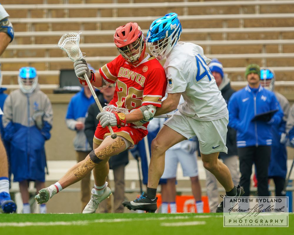 Lacrosse players battle for ball possession during intense game action with red and white uniforms.