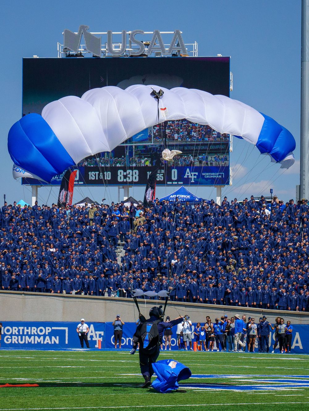 Parachutist lands on blue football field during stadium event with packed crowd.