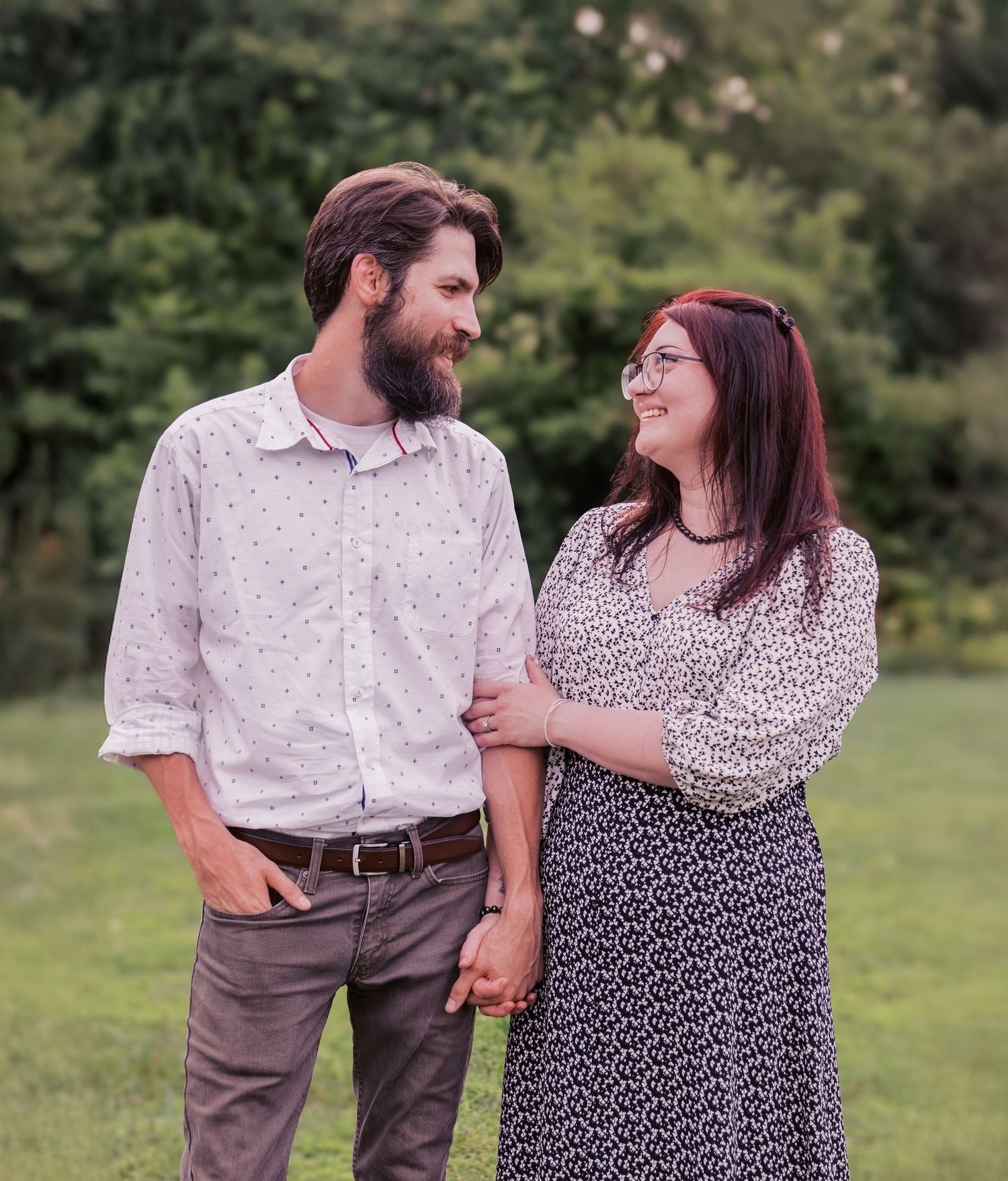 Couple in casual attire sharing loving glances and holding hands outdoors.