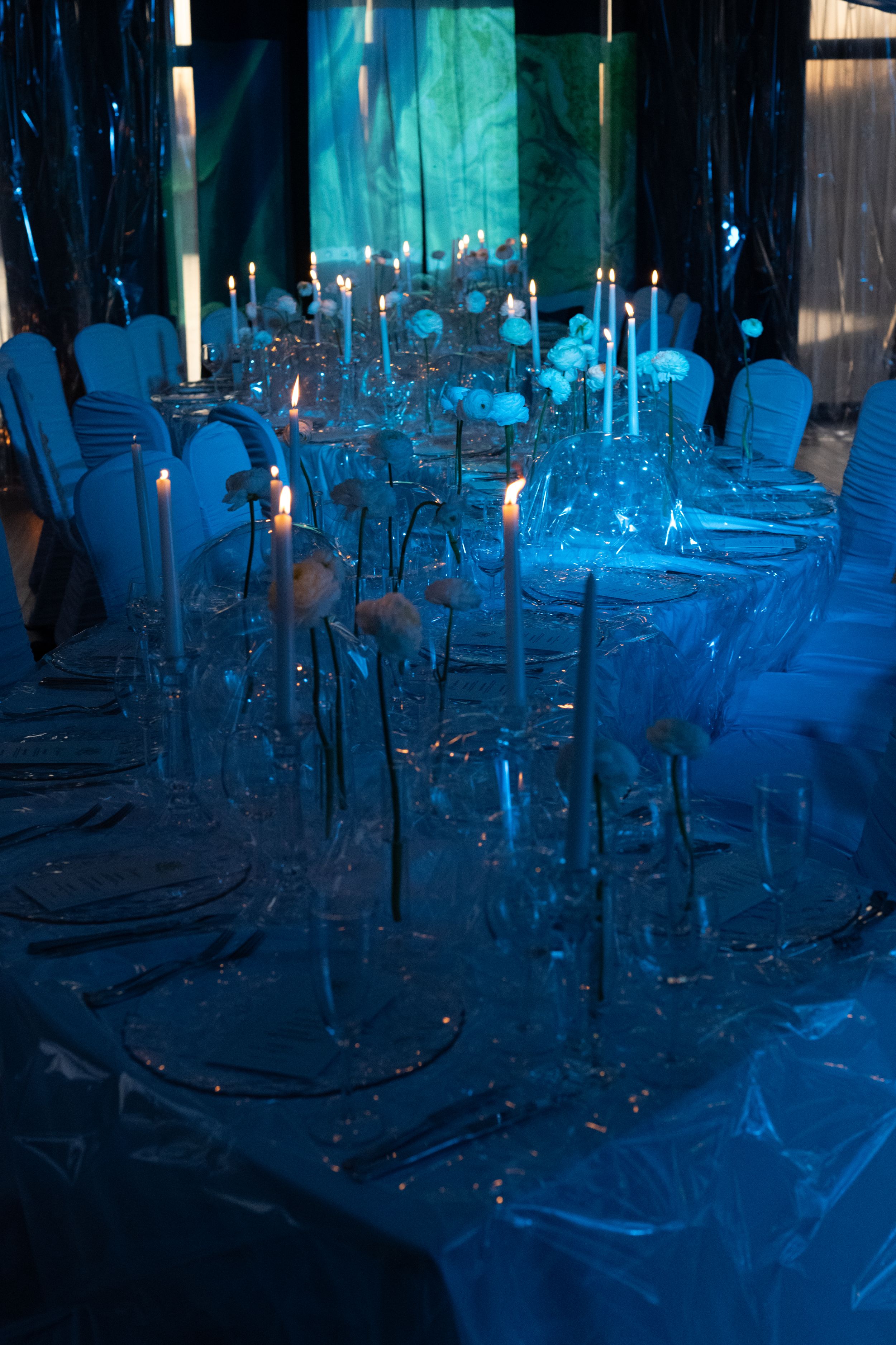Elegant banquet table setting with blue uplighting and tall white candles creating a magical aquatic atmosphere.