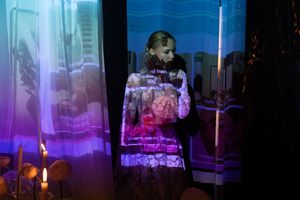 A dark atmospheric scene lit with blue and purple neon lights showing someone surrounded by glass displays.