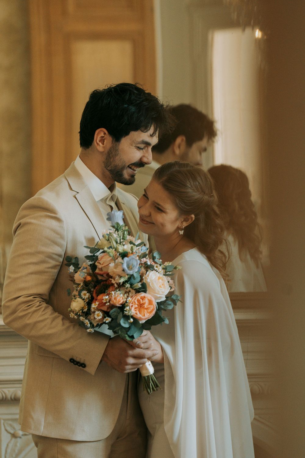 Romantic couple in wedding attire share intimate moments while holding floral bouquets in warm indoor lighting.