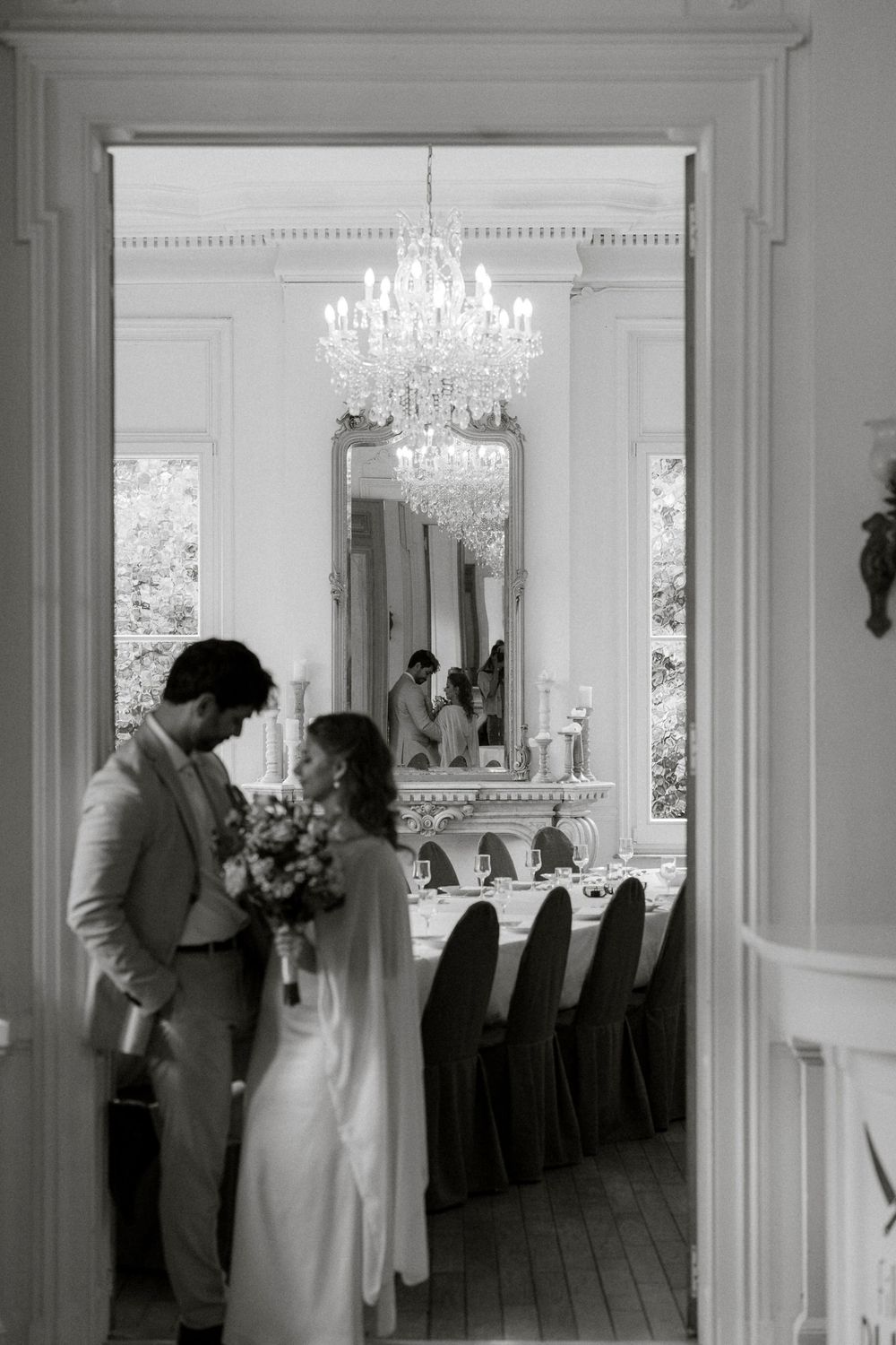 Elegant wedding reception setup in a bright white ballroom with crystal chandeliers and tall windows.
