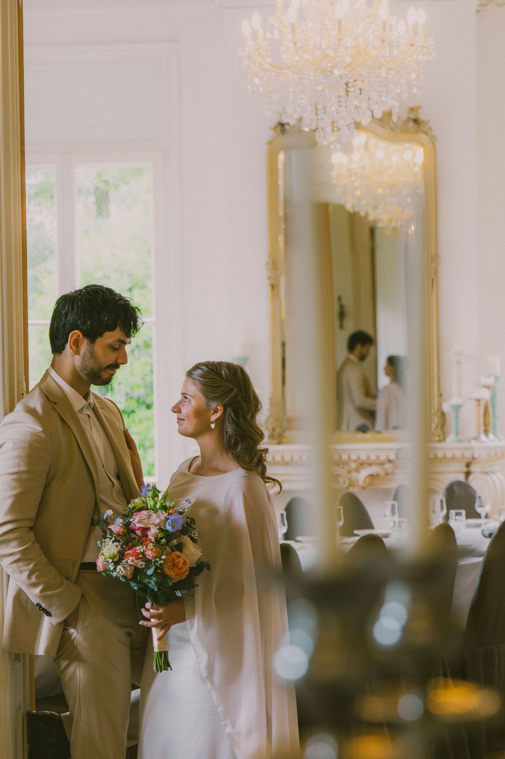 A romantic wedding moment captured in an elegant room with crystal chandeliers and soft natural lighting.