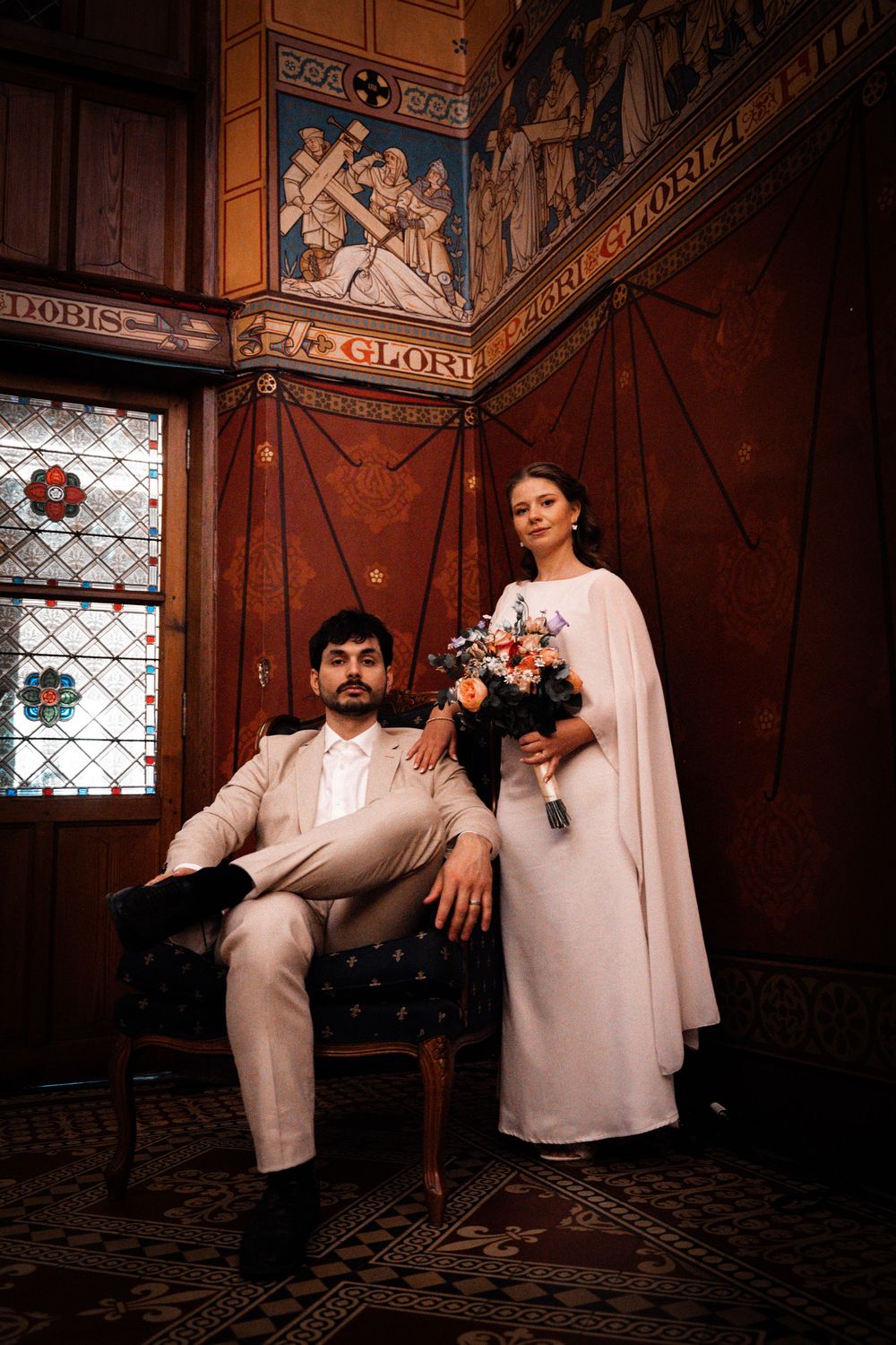 A wedding portrait in a gothic interior with stained glass and wooden paneling.