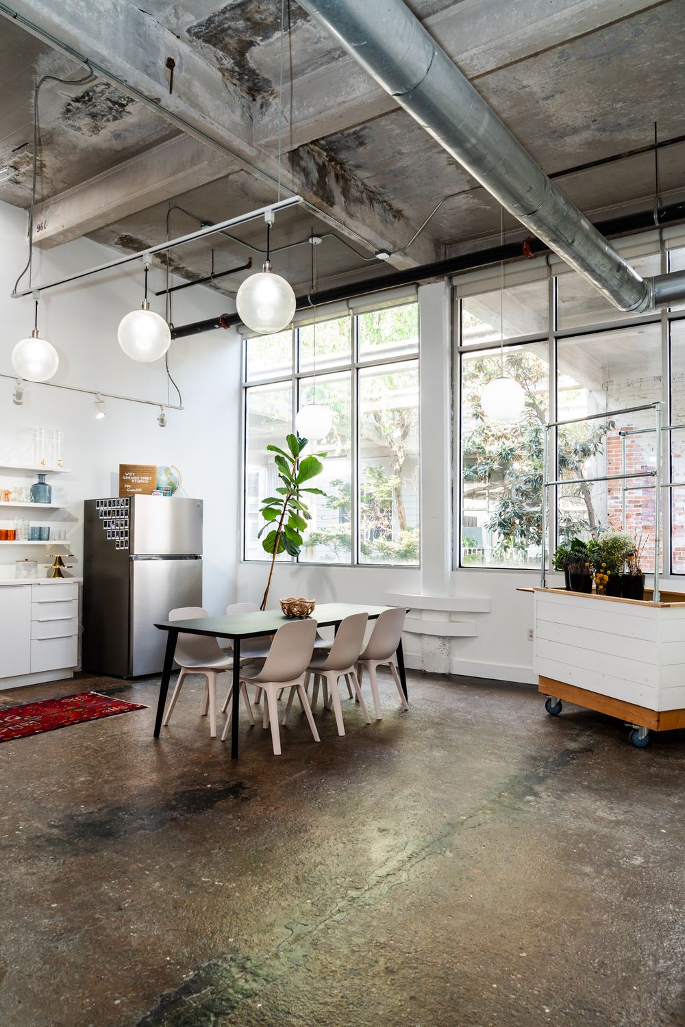 Industrial style dining area with concrete floors, white walls, and modern pendant lighting.