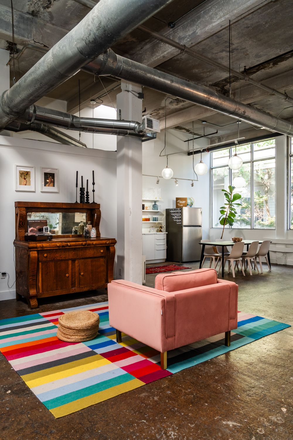 Industrial loft space with pink armchair, colorful rug, and vintage furniture.
