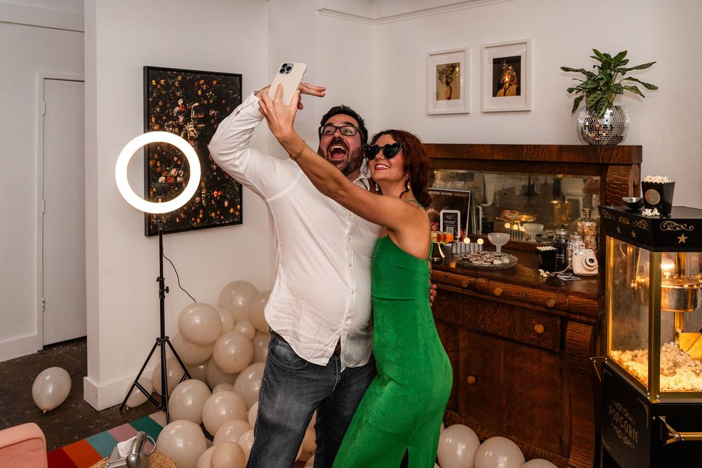 Two people taking selfies with ring light in decorated room.